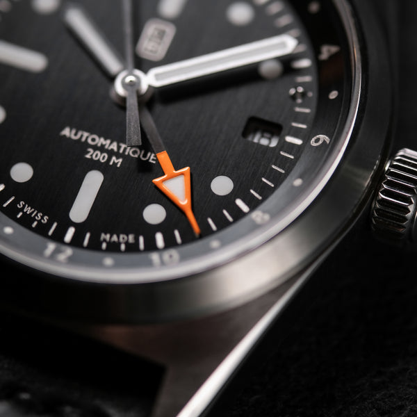 The orange tip of the GMT hand. Macro photography. Swiss made written on the black dial