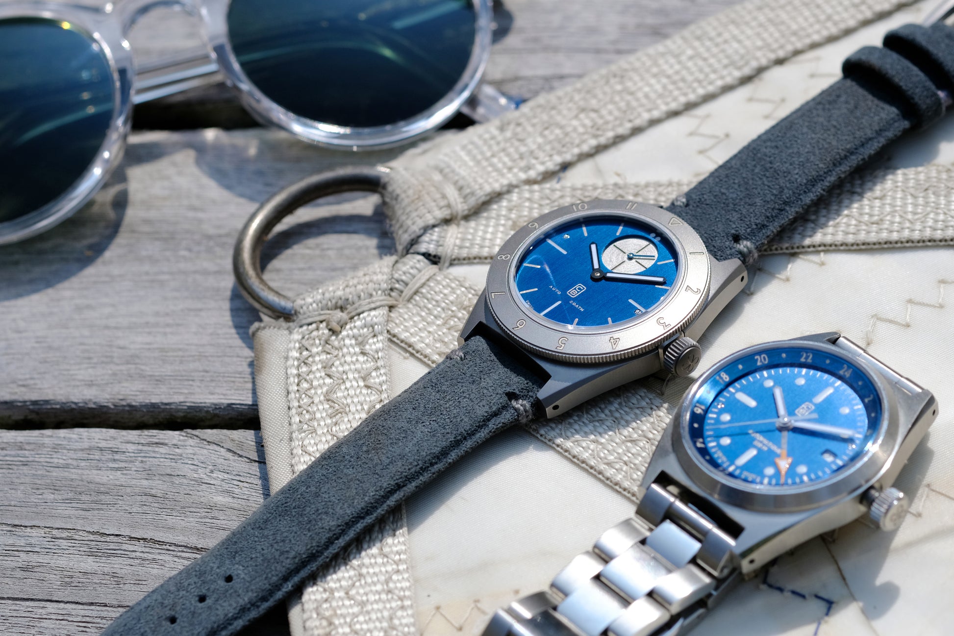 Sustainable watches on a boat canvas, summer vibes, blue dials taking the sun and reveal beautiful blue contrasts. Repurposed titanium for left hand watch, 100% recycled stainless steel for the right GMT watch