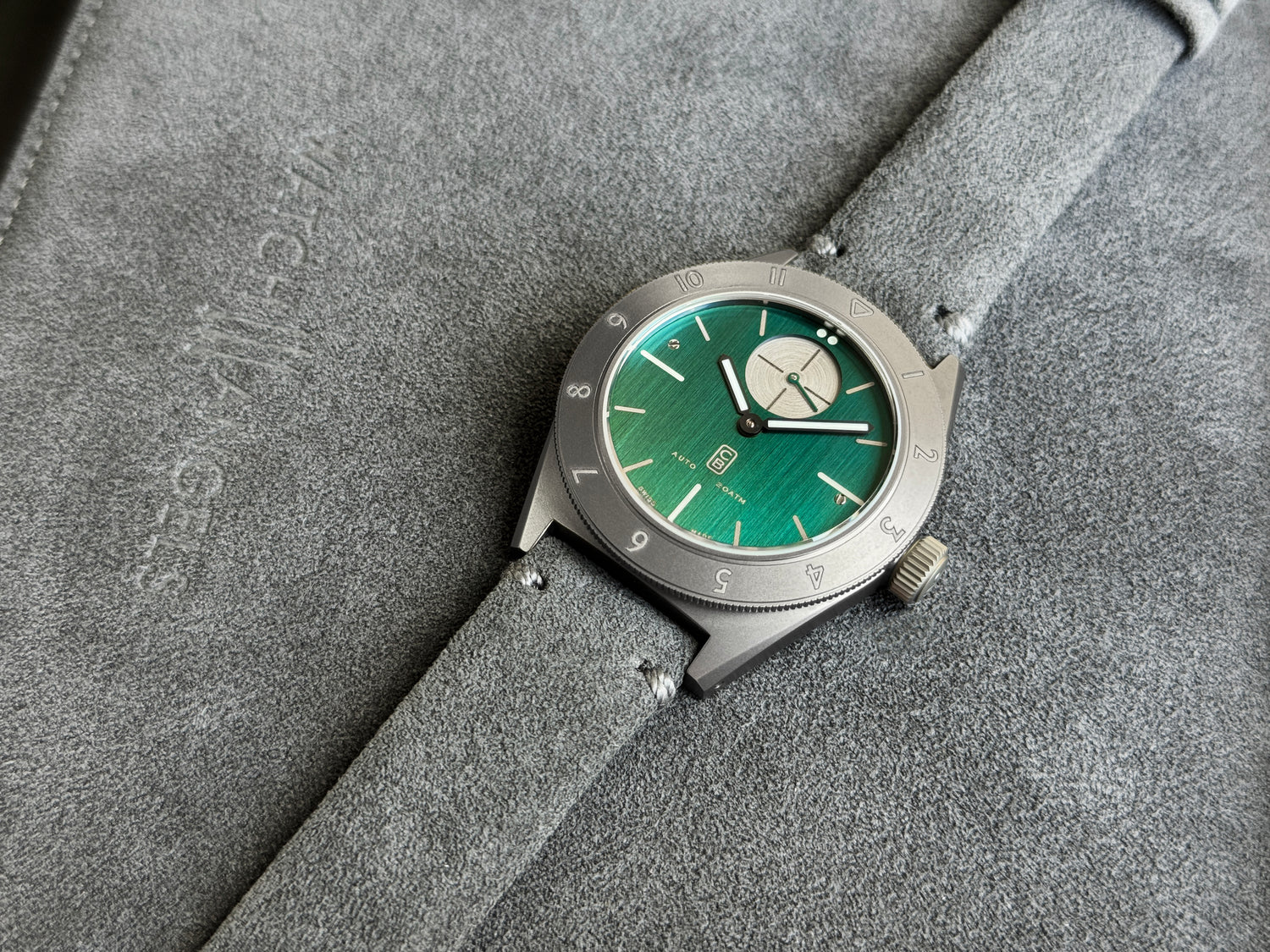 GMT automatic watch, with a deep green dial made of repurposed titanium for maximum sustainability, alcantara strap on alcantara pouch