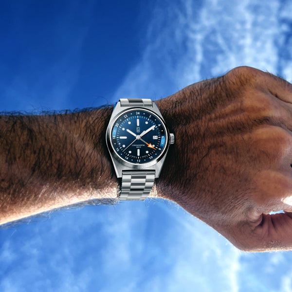 Blue dial CB01-GMT watch worn on the wrist, blue sky and few clouds as background