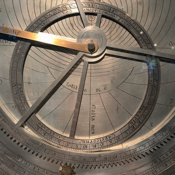 Ancient metal astrolabe, a circular astronomical instrument with engraved plates and a rotating star map, used to measure the position of stars, determine time and latitude, and emblematic of medieval navigation and science.
