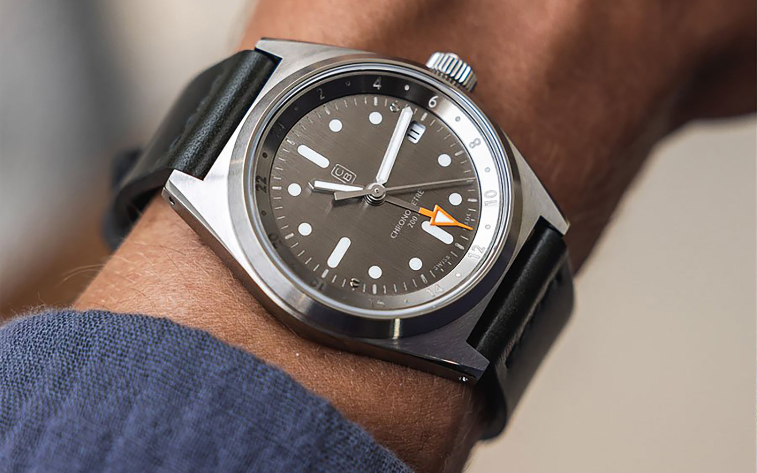 Raw and naked dial of the Cedric Bellon CB01 GMT with its orange hand tip, worn on a wrist